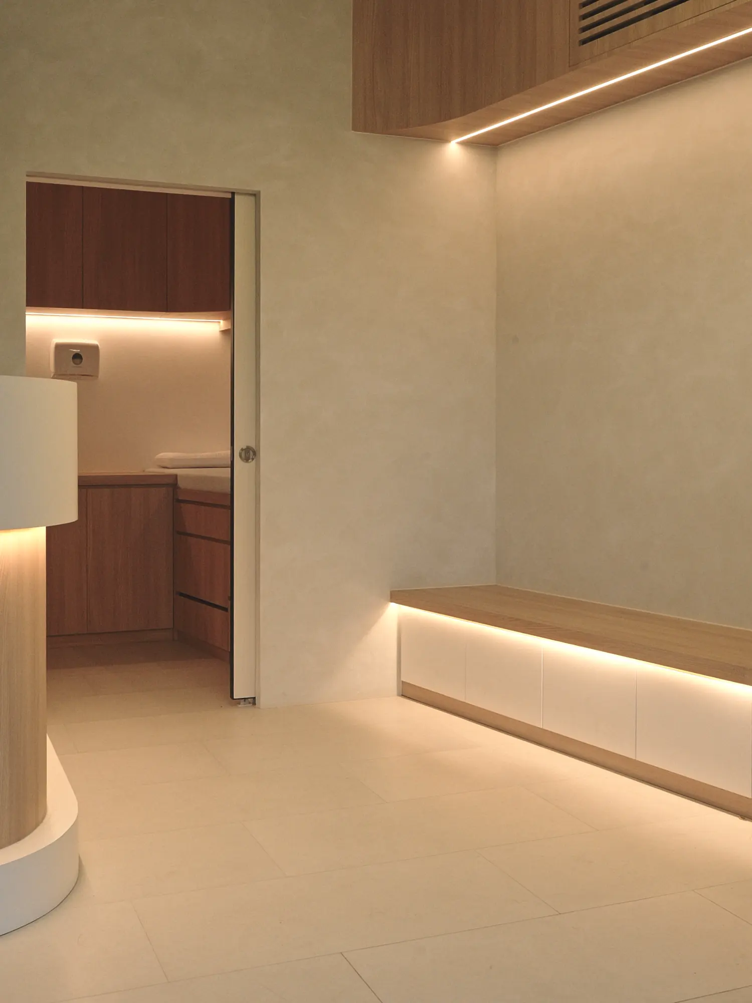 The waiting area, a floating timber bench beneath a cove-lit wall